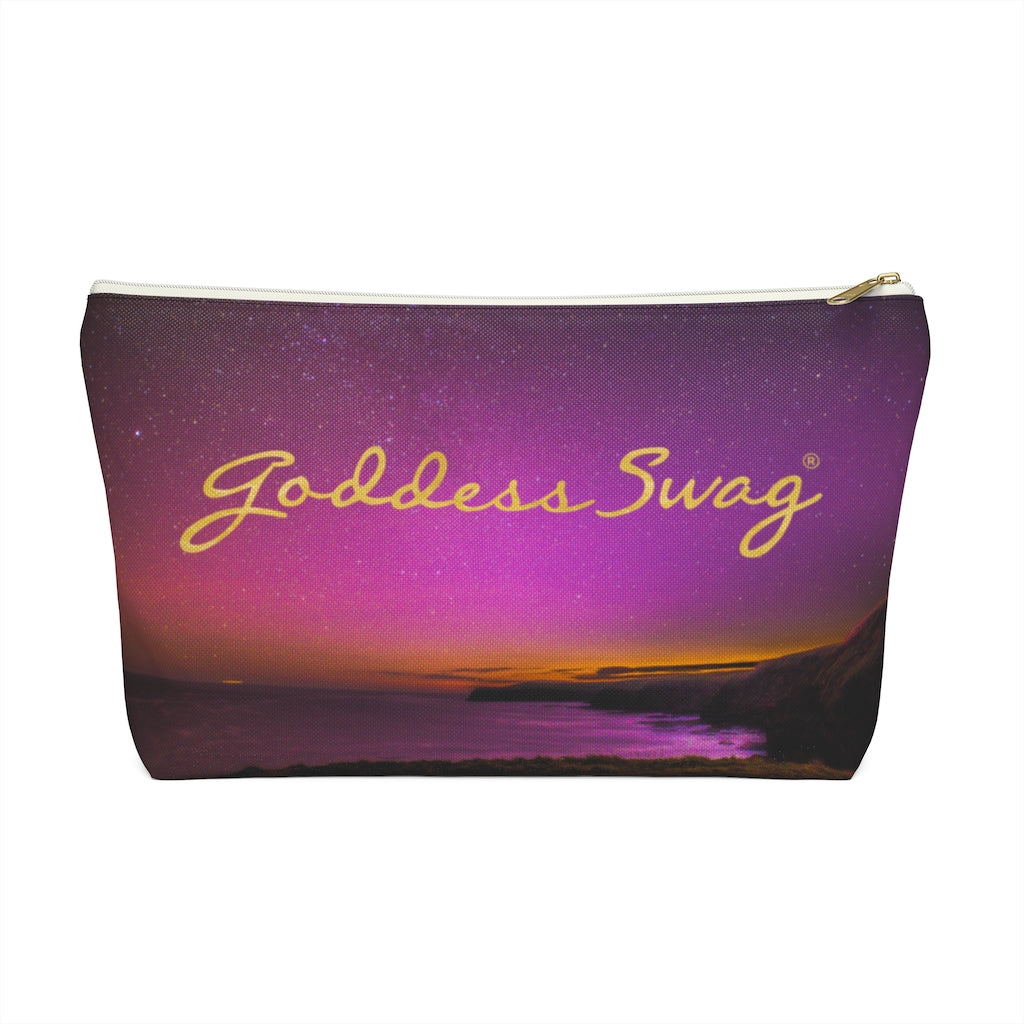 Goddess Swag Bag Mini (named cosmic).  Item can be used as accessory pouch, makeup bag or cosmetic bag with a background is purple with some orange like sunset.  Goddess Swag wording is in gold on one side of the bag only.  There is an option of a black or a white zipper, and a large or a small bag. 