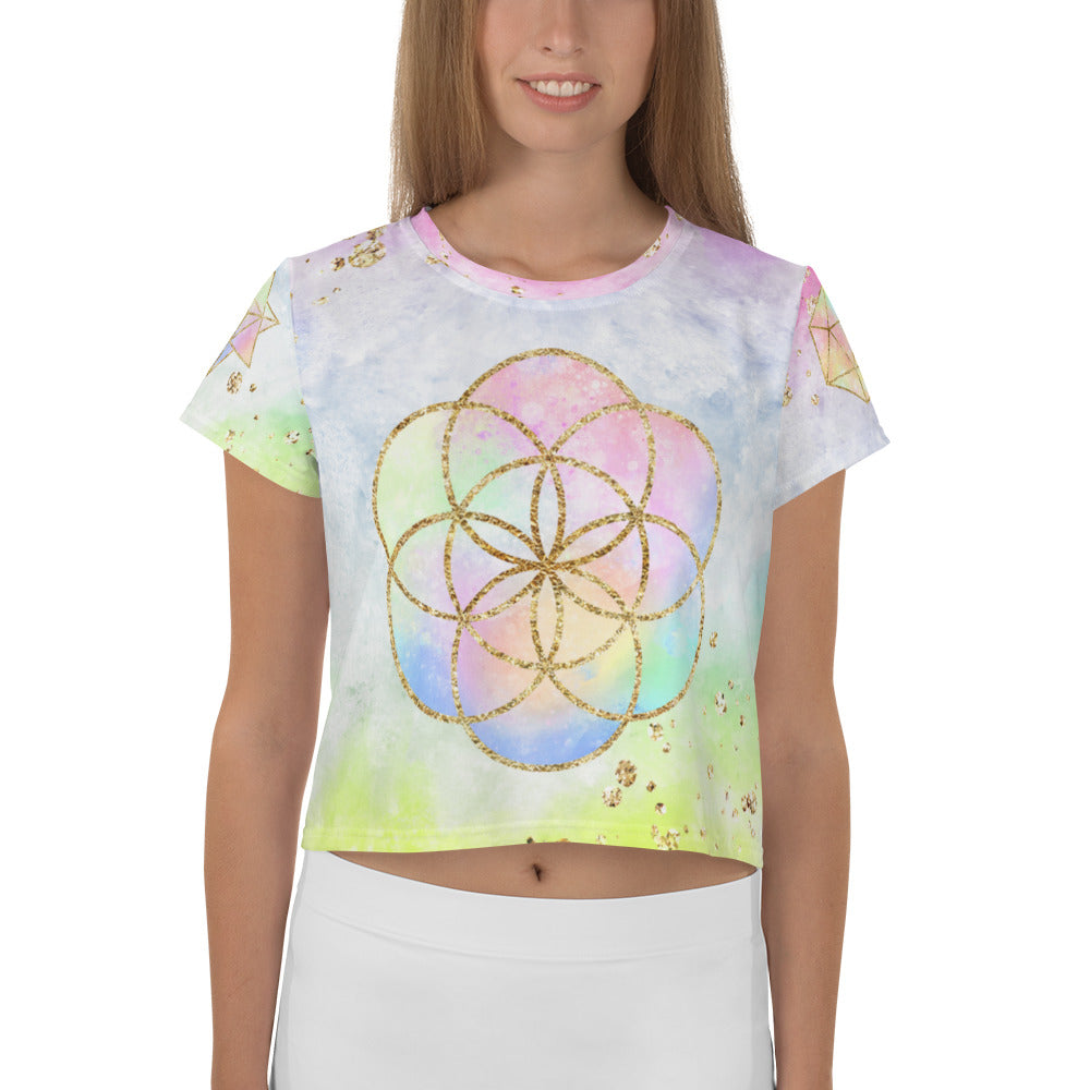 short sleeve crop top tee shirt pastel tie dye background with seed of life design in gold  on front.  Left sleeve has a hexagon and right has a star tetrahedron symbol.
