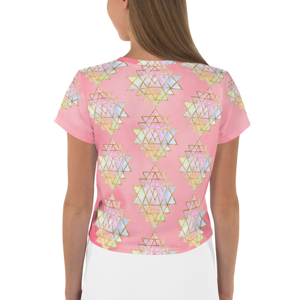 Light to medium pink background with pastel and gold color sri yantra design all over front back and short sleeves.  This is a crop top tee by goddess swag as part of the cosmic powers collection