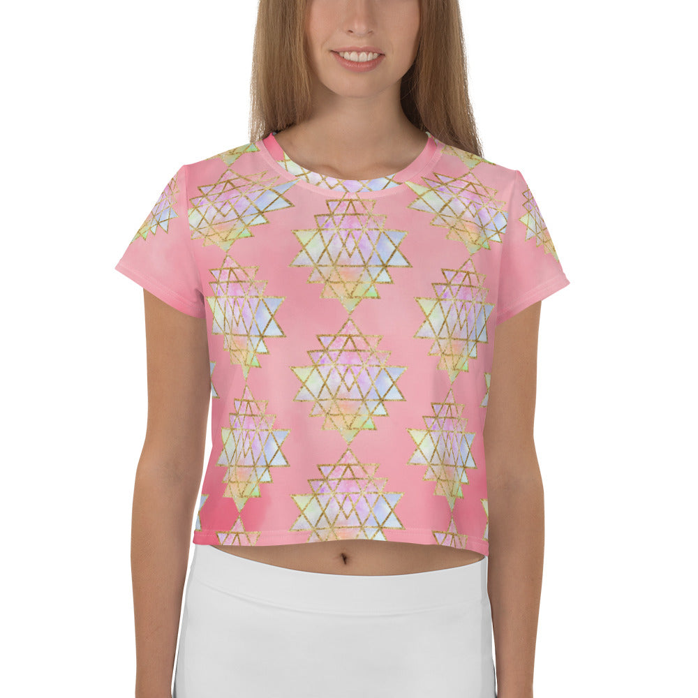 Light to medium pink background with pastel and gold color sri yantra design all over front back and short sleeves.  This is a crop top tee by goddess swag as part of the cosmic powers collection