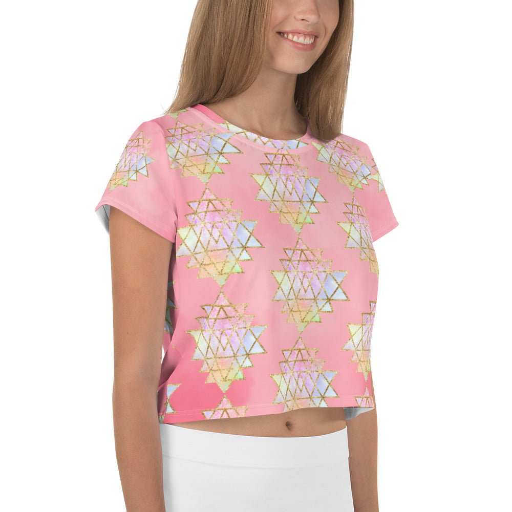Light to medium pink background with pastel and gold color sri yantra design all over front back and short sleeves.  This is a crop top tee by goddess swag as part of the cosmic powers collection