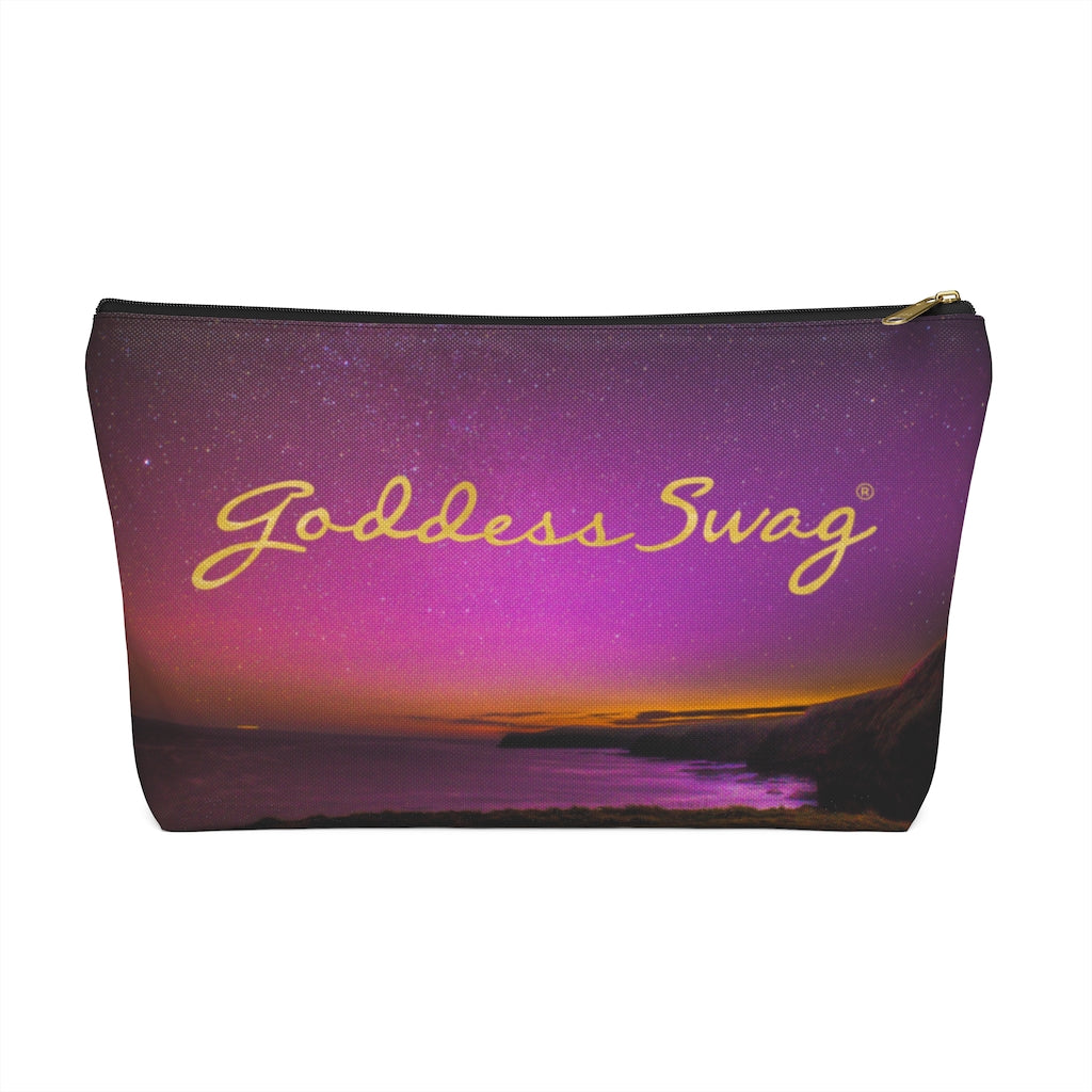 Goddess Swag Bag Mini (named cosmic).  Item can be used as accessory pouch, makeup bag or cosmetic bag with a background is purple with some orange like sunset.  Goddess Swag wording is in gold on one side of the bag only.  There is an option of a black or a white zipper, and a large or a small bag. 