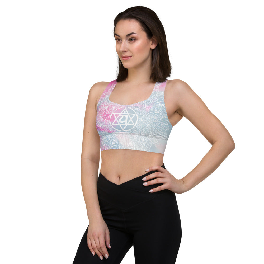 longline sports bra by goddess swag. main colors are pastel pinks and blues. the design overlay on front and back is a white heart chakra mandala design. goddess swag is written on the back in sanskrit style writing