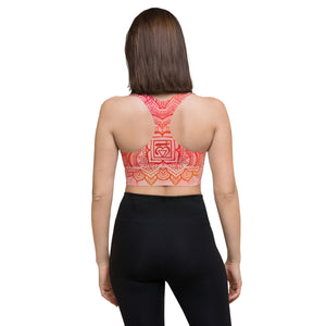 longline sports bra by goddess swag. the design has a pink orange background with an overlay of a root chakra mandala design in red and orange. this design is on front and back of sports bra.