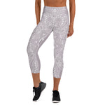 Load image into Gallery viewer, mystic-77-heart-chakra-mandala-capri-leggings-by-goddess-swag.  Background color is a light to medium mauve.  The mandala design is white and all over front and back. Goddess Swag is written on the back waistband in sanskrit style in a deep purple.
