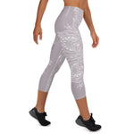 Load image into Gallery viewer, mystic-77-heart-chakra-mandala-capri-leggings-by-goddess-swag.  Background color is a light to medium mauve.  The mandala design is white and all over front and back. Goddess Swag is written on the back waistband in sanskrit style in a deep purple.
