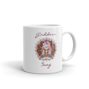 Goddess Swag, ceramic coffee mug 11 ounces. Goddess with Mandala behind her and seven colorful chakras from root to crown. She is sitting in lotus position. Goddess Swag which is written in deep purple color.